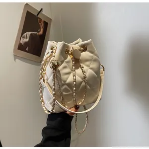 Close-up of cream quilted bucket bag with gold chain strap and spherical charm
