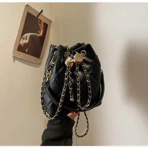 Close-up of black quilted bucket bag with gold chain drawstrings and tassel detail