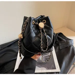 Macro detail of black quilted bucket bag with gold chain strap and drawstring metal orb