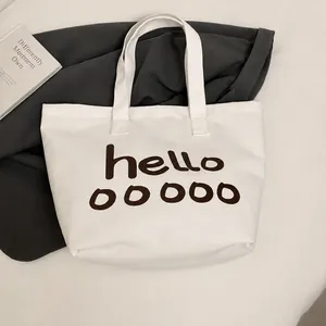 Primer plano de un bolso tote de lona blanca con texto artístico hello ooooo en tela gris