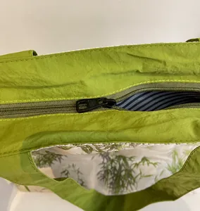 Detail of smooth metal zipper and blue striped lining on green nylon tote bag