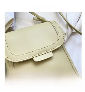 Detail of smooth leather texture and fine stitching on a pale yellow mini crossbody bag