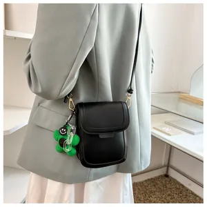 Chic black mini crossbody phone bag with green plush bear charm on a female model