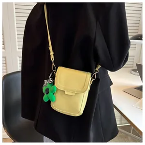 Mini crossbody phone bag in pale yellow with a green floral charm on a black blazer