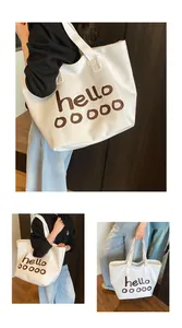 Detailopname van witte canvas draagtas met hello-print en brede schouderband