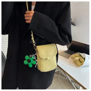Detailed close-up of a mini leather crossbody phone bag with a green floral charm