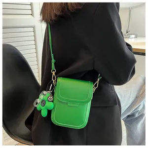 Detail view of bright green mini crossbody bag with a floral plush charm on a black blazer