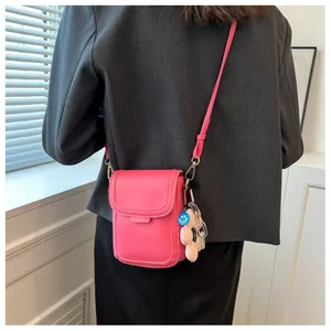 Bright pink crossbody mobile phone bag with decorative charms worn over a grey blazer