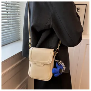 Detail of cream crossbody phone bag with gold clasp and blue sunflower charm on a model