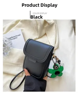 Detail of a black mini crossbody bag with a green flower charm on a lifestyle background