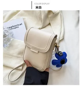 Close-up of off-white leather phone bag with a blue flower charm and smiley face
