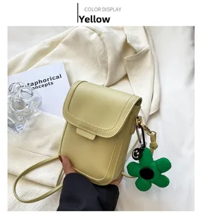 Close-up of a yellow mini crossbody phone bag with a green flower charm on a white background