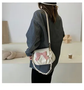 Détail du sac bandoulière plissé crème avec nœud rose et poignée tressée porté à l'épaule
