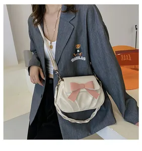 Détail d'un sac bandoulière plissé crème avec un nœud rose mat et bandoulière