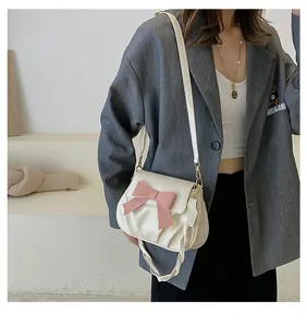 Détail du sac plissé crème avec un grand nœud rose sur un blazer blanc cassé