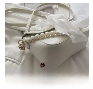 Detail of white leather crossbody bag with faux pearl handle and large organza bow decoration