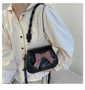 Détail du sac bandoulière noir avec un nœud marron et une bandoulière tressée