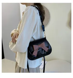 Détail d'un sac bandoulière en similicuir noir avec nœud marron et bandoulière tressée