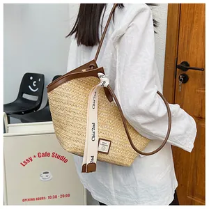 Detail of straw bucket bag with brown leather trim and shoulder strap in a cafe setting