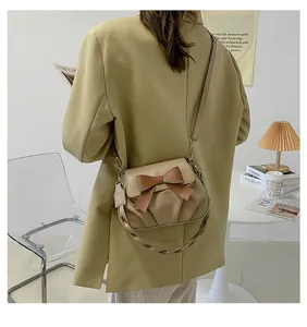 Vue portée d'un sac bandoulière beige plissé avec nœud marron et poignée tressée