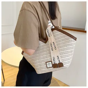 Detail view of woven straw tote bag featuring brown leather trim and stylish lettered strap