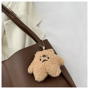 Close-up of a cute khaki plush star charm with silver chain on a brown leather bag