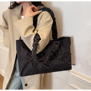 Detail of black nylon tote bag featuring ruffled handles and white bow embroidery