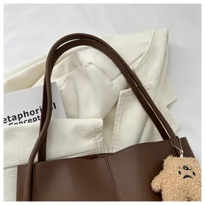 Detail of dark brown matte PU tote bag featuring a cute plush bear charm on the side