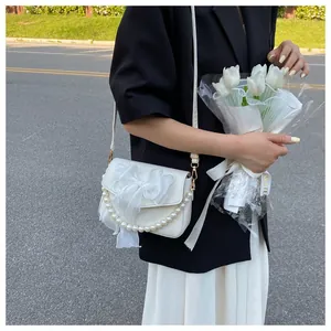 Detail of white crossbody bag featuring oversized gauze bow and pearl handle strap