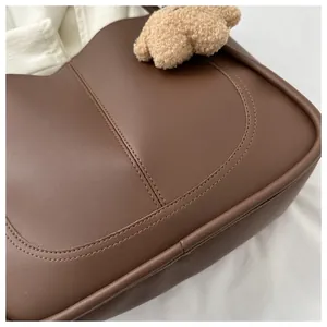 Detail of dark brown PU leather tote with curved stitching and plush bear charm