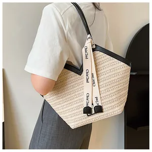 Detail of a large straw tote bag with black leather handles and woven ribbon detail