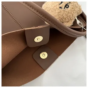 Close-up of brown PU tote bag showing magnetic snap closure and cute plush bear charm
