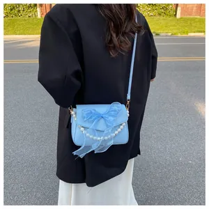 Detail of light blue crossbody bag with organza bow and pearl accents on a model