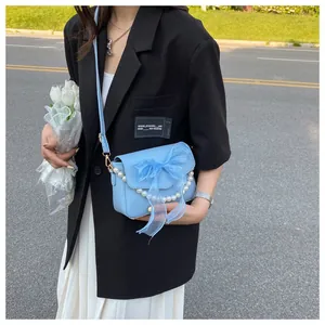 Close-up of light blue crossbody bag with mesh bow and decorative pearl chain detail