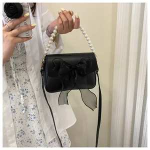 Detail of black crossbody bag with mesh bow and large white pearl handle on female model