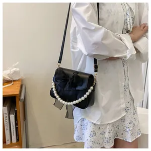 Detail of black crossbody bag featuring a large tulle bow and pearl decorative handle