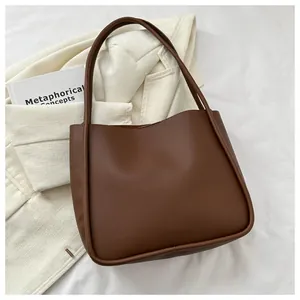 Deep brown matte faux leather tote bag displayed with a cream blazer and art book