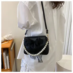 Detail of black crossbody bag with mesh bow decoration and pearl handle on a model