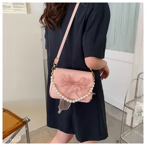 Detail of pink crossbody bag with a tulle bow, large pearl chain, and leather texture