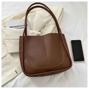 Flat lay of a brown PU leather tote bag styled with a white blazer and books