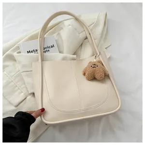 Detail of creamy white PU leather tote bag with U-shaped stitching and bear charm
