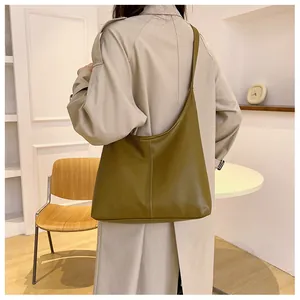 Olive green tote bag with smooth faux leather texture shown on shoulder in a cozy interior