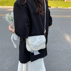 Elegant white crossbody bag with lace bow and pearl chain shown in outdoor street style