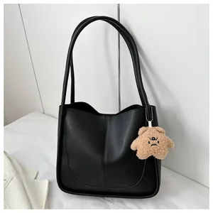 Detail of black PU leather tote bag featuring U-shaped stitching and plush bear charm