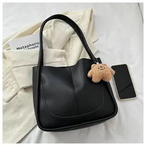 Detail of black PU leather tote bag with U-shaped stitching and cute brown bear charm