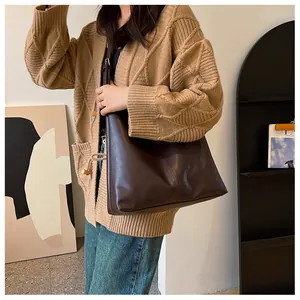 Brown leather tote bag featuring a vertical seam detail worn with a beige cardigan