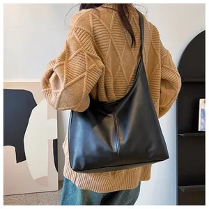 Rear view of black minimalist leather tote bag showing smooth texture on beige knitwear