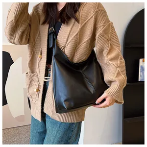 Close-up of black textured leather shoulder bag worn with casual knitted cardigan