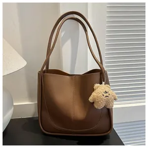 Detailed view of caramel PU tote bag featuring a cute plush bear pendant accessory