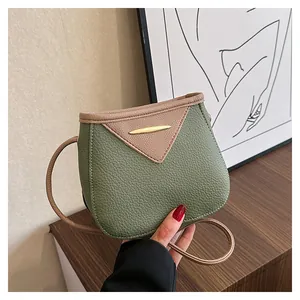 Detail view of pink V-flap closure with gold clasp on green textured leather crossbody bag